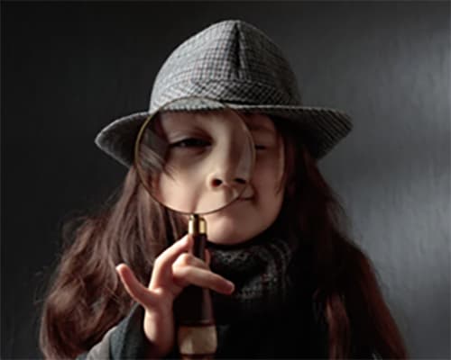 A child holding up a magnifying glass up to their eye as if looking for a clue.